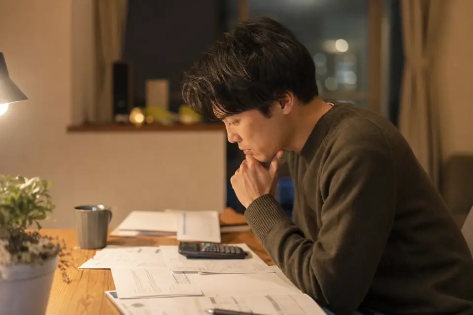 机の上で料金の書類と電卓を見比べている人のイメージ写真